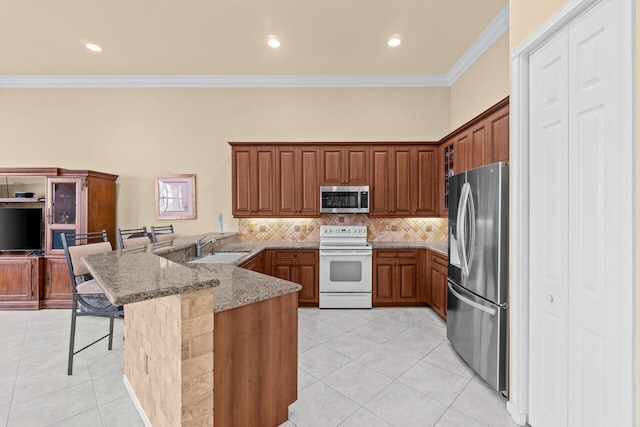 kitchen featuring a breakfast bar, brown cabinets, stainless steel appliances, light tile patterned flooring, and a peninsula