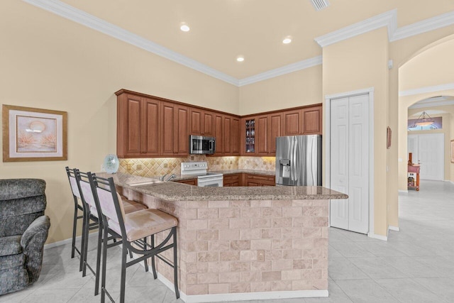 kitchen with arched walkways, appliances with stainless steel finishes, glass insert cabinets, a peninsula, and crown molding