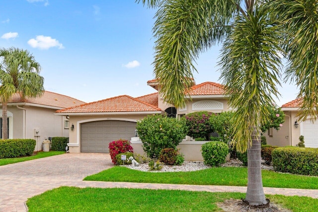 mediterranean / spanish-style home featuring a garage, a tiled roof, decorative driveway, a front lawn, and stucco siding