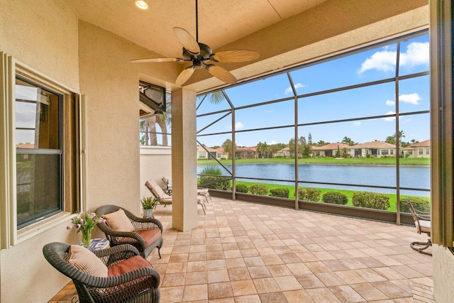 sunroom featuring a ceiling fan, a residential view, and a water view