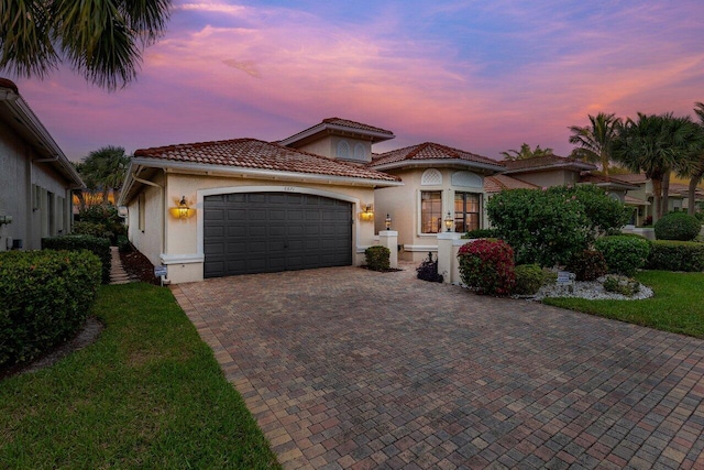 mediterranean / spanish house with a tiled roof, an attached garage, decorative driveway, french doors, and stucco siding