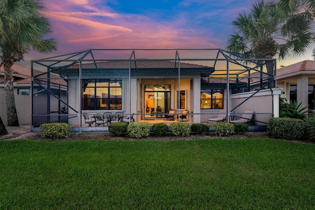 rear view of house with a yard, a tiled roof, a patio area, and glass enclosure