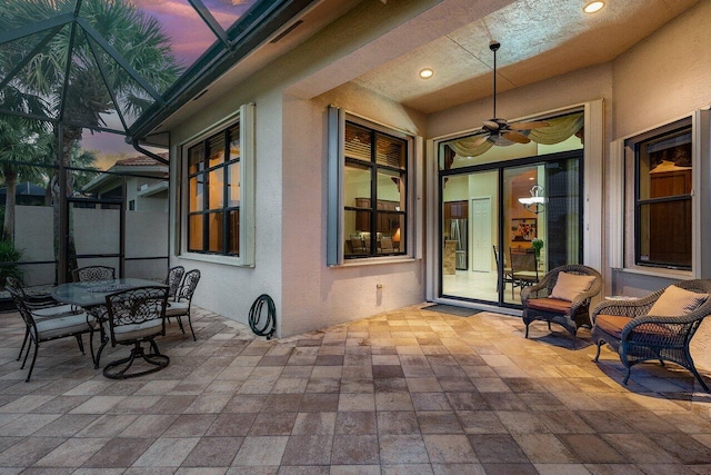 patio terrace at dusk featuring glass enclosure, ceiling fan, and outdoor dining area