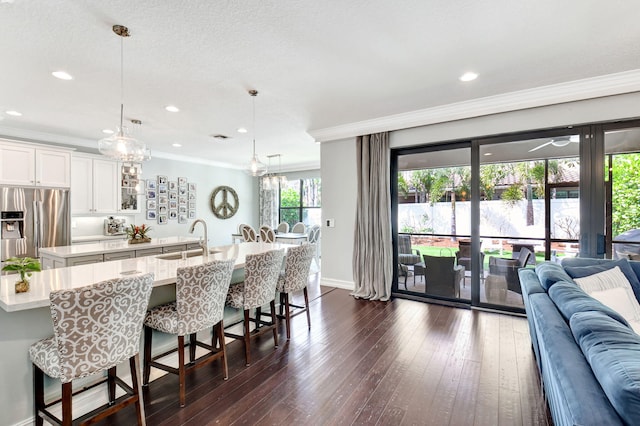 kitchen featuring a sink, open floor plan, stainless steel fridge, a center island with sink, and crown molding