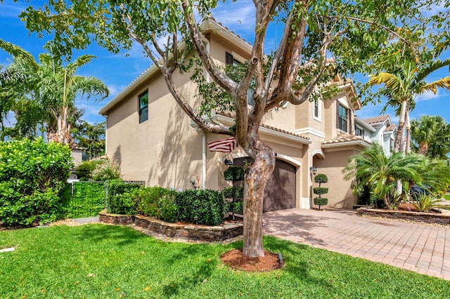 view of front facade with a garage, a tile roof, decorative driveway, stucco siding, and a front lawn