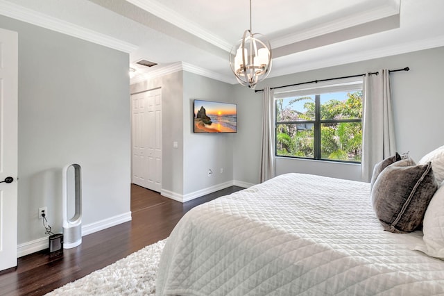 bedroom featuring baseboards, a raised ceiling, ornamental molding, wood finished floors, and a chandelier