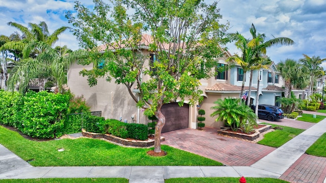 view of front of house featuring decorative driveway, a tile roof, stucco siding, a garage, and a front lawn