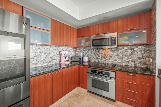 kitchen with decorative backsplash, dark stone counters, brown cabinetry, and stainless steel appliances