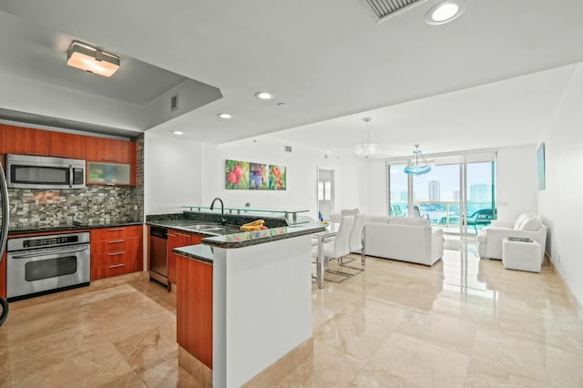 kitchen featuring a sink, open floor plan, a peninsula, appliances with stainless steel finishes, and decorative backsplash