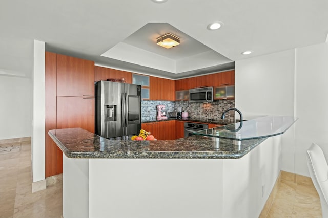 kitchen with dark stone countertops, stainless steel appliances, a raised ceiling, modern cabinets, and brown cabinets