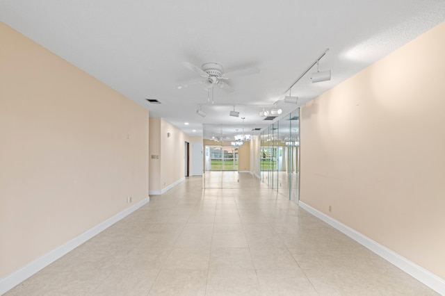 hallway with light tile patterned floors, visible vents, baseboards, and track lighting