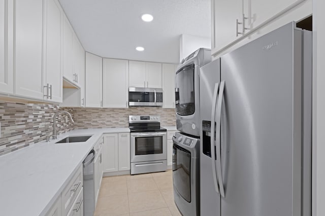 kitchen featuring light countertops, stacked washer and clothes dryer, appliances with stainless steel finishes, light tile patterned flooring, and a sink