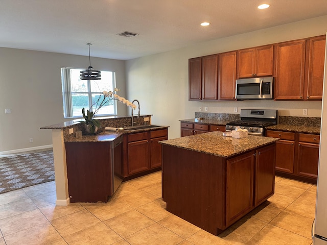 kitchen featuring visible vents, an island with sink, appliances with stainless steel finishes, dark stone countertops, and a sink