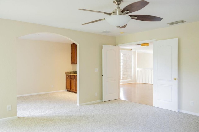 spare room featuring arched walkways, visible vents, light carpet, and baseboards