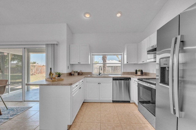 kitchen featuring light tile patterned floors, a peninsula, appliances with stainless steel finishes, and a sink