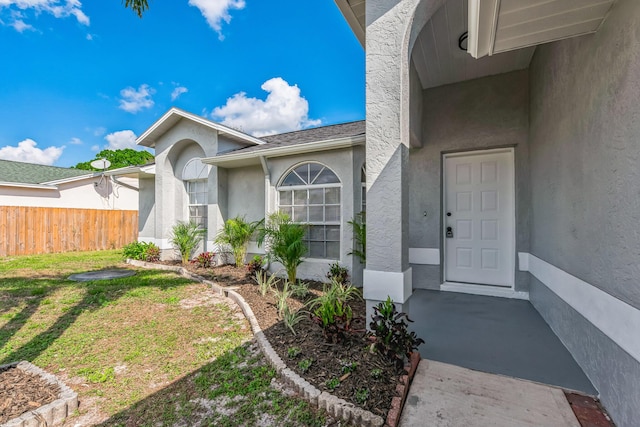 doorway to property with a yard, fence, and stucco siding