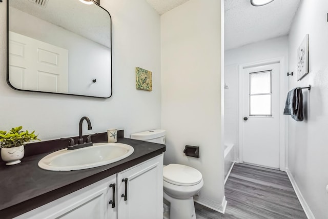 full bathroom featuring a textured ceiling, vanity, toilet, and wood finished floors