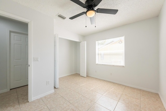 unfurnished bedroom featuring a textured ceiling, ceiling fan, light tile patterned flooring, visible vents, and baseboards