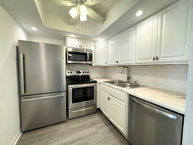 kitchen featuring a tray ceiling, light wood-style flooring, decorative backsplash, appliances with stainless steel finishes, and a sink