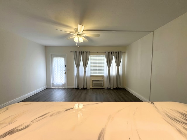 unfurnished bedroom with ceiling fan, dark wood-style flooring, a wall mounted AC, and baseboards