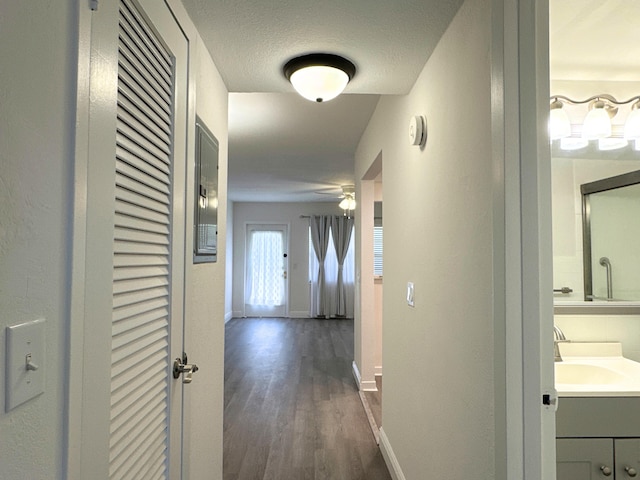 hallway with dark wood-style floors, a textured ceiling, a sink, and baseboards