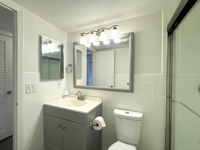 bathroom with toilet, a shower with shower door, tile walls, and vanity