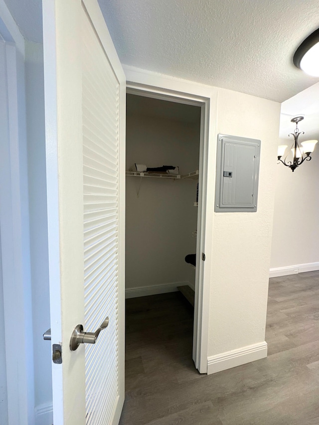 hallway with a notable chandelier, a textured ceiling, wood finished floors, electric panel, and baseboards