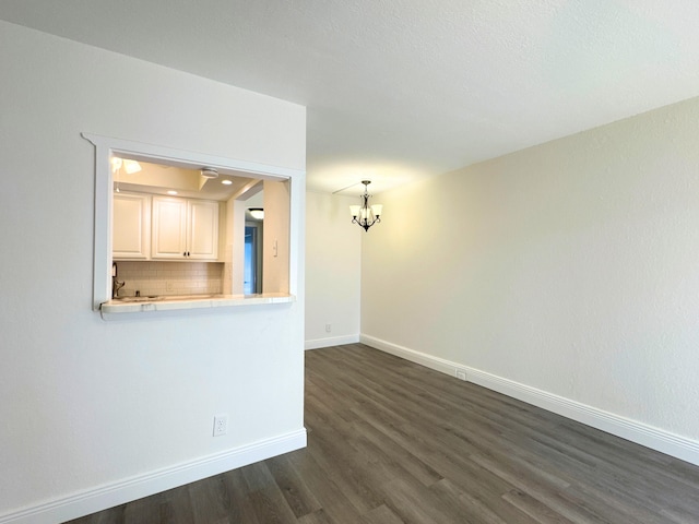 spare room with dark wood-style floors, an inviting chandelier, and baseboards