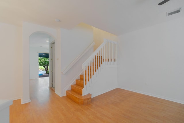 staircase featuring arched walkways, wood finished floors, visible vents, and baseboards