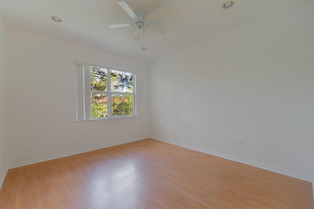 spare room featuring light wood-type flooring, a ceiling fan, and baseboards