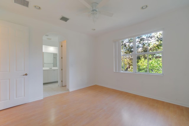 spare room with light wood-style floors, baseboards, visible vents, and arched walkways