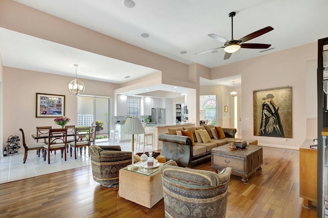 living room with baseboards, wood finished floors, and ceiling fan with notable chandelier