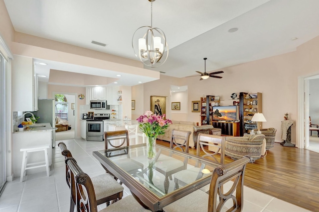 dining space with light tile patterned floors, ceiling fan with notable chandelier, and visible vents