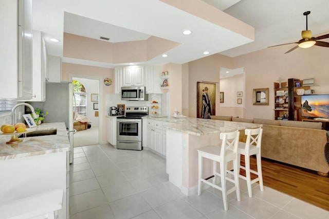 kitchen with a peninsula, a sink, stainless steel appliances, a kitchen bar, and open floor plan