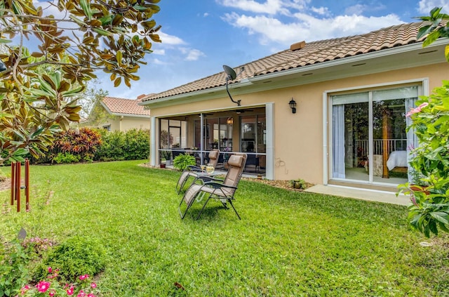 back of property featuring a yard, a sunroom, stucco siding, and a tile roof