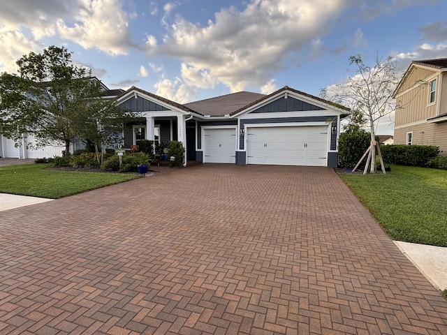 view of front of home with a front yard, board and batten siding, decorative driveway, and an attached garage