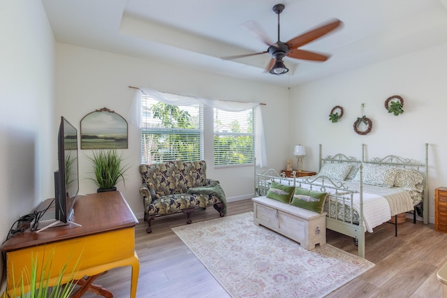 bedroom with a tray ceiling, light wood-type flooring, a ceiling fan, and baseboards