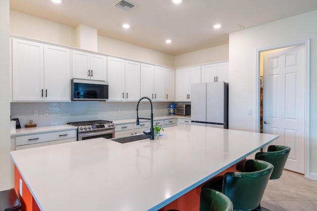 kitchen with freestanding refrigerator, white cabinetry, a breakfast bar, gas range, and a sink