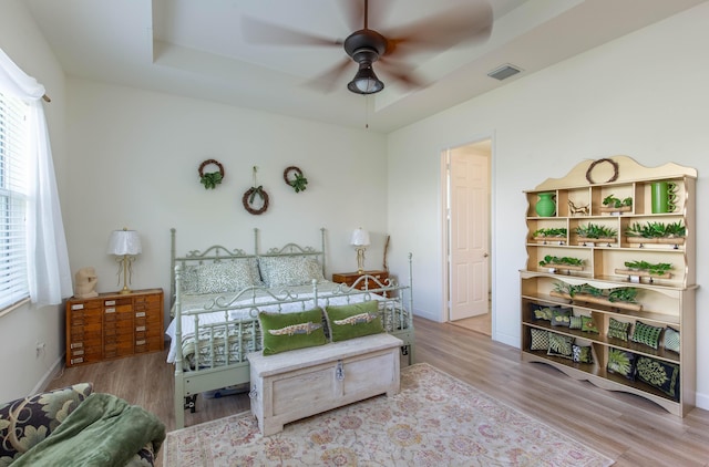 bedroom with baseboards, visible vents, a raised ceiling, and wood finished floors