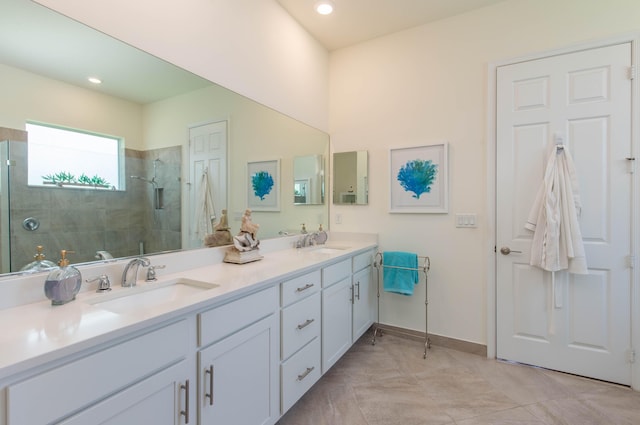 full bath featuring double vanity, tiled shower, a sink, and baseboards