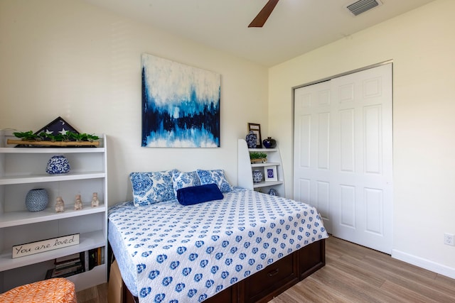 bedroom with wood finished floors, visible vents, baseboards, a ceiling fan, and a closet