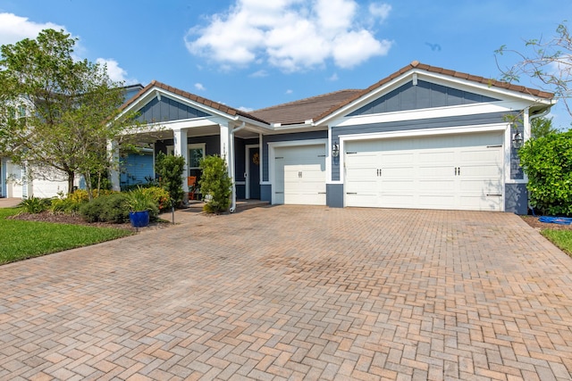 view of front of home with board and batten siding, a garage, decorative driveway, and a tiled roof