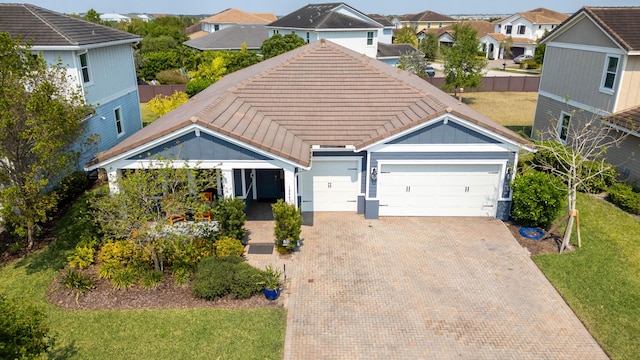 view of front of home with decorative driveway, a tile roof, a garage, a residential view, and a front lawn