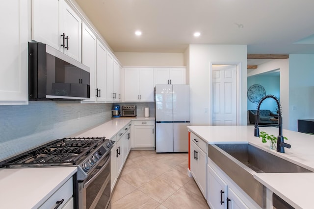 kitchen with stainless steel gas range oven, tasteful backsplash, freestanding refrigerator, white cabinetry, and a sink