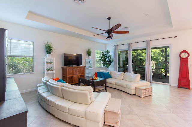 living room with a tray ceiling, baseboards, a ceiling fan, and light tile patterned floors