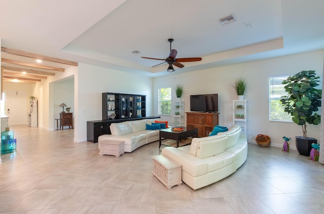 living area with a tray ceiling, a ceiling fan, visible vents, light tile patterned flooring, and baseboards
