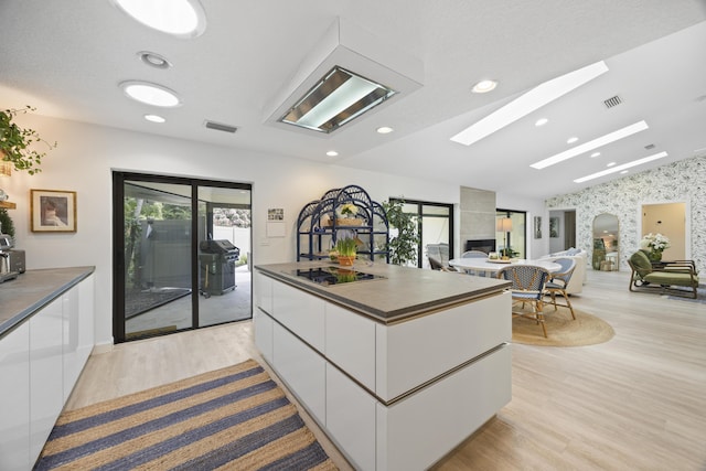 kitchen featuring dark countertops, a center island, vaulted ceiling with skylight, white cabinets, and modern cabinets