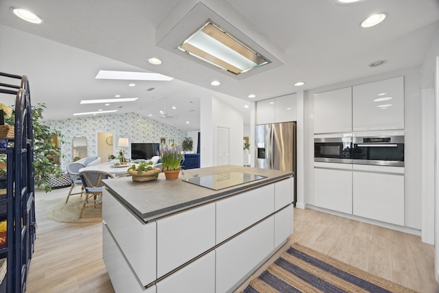 kitchen with modern cabinets, white cabinetry, vaulted ceiling with skylight, appliances with stainless steel finishes, and wallpapered walls