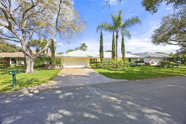 single story home with an attached garage, decorative driveway, and a front lawn