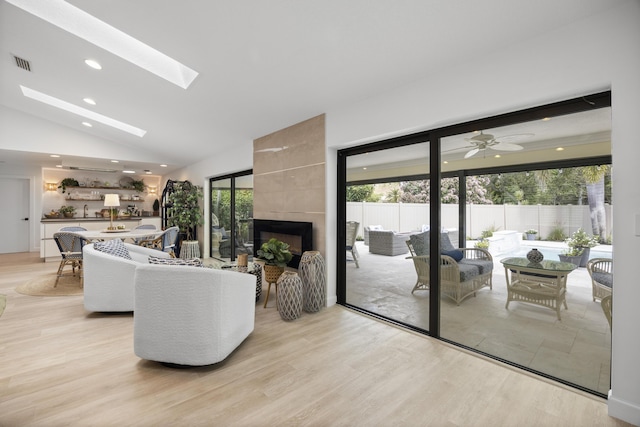 living room featuring light wood-type flooring, visible vents, lofted ceiling with skylight, recessed lighting, and a fireplace